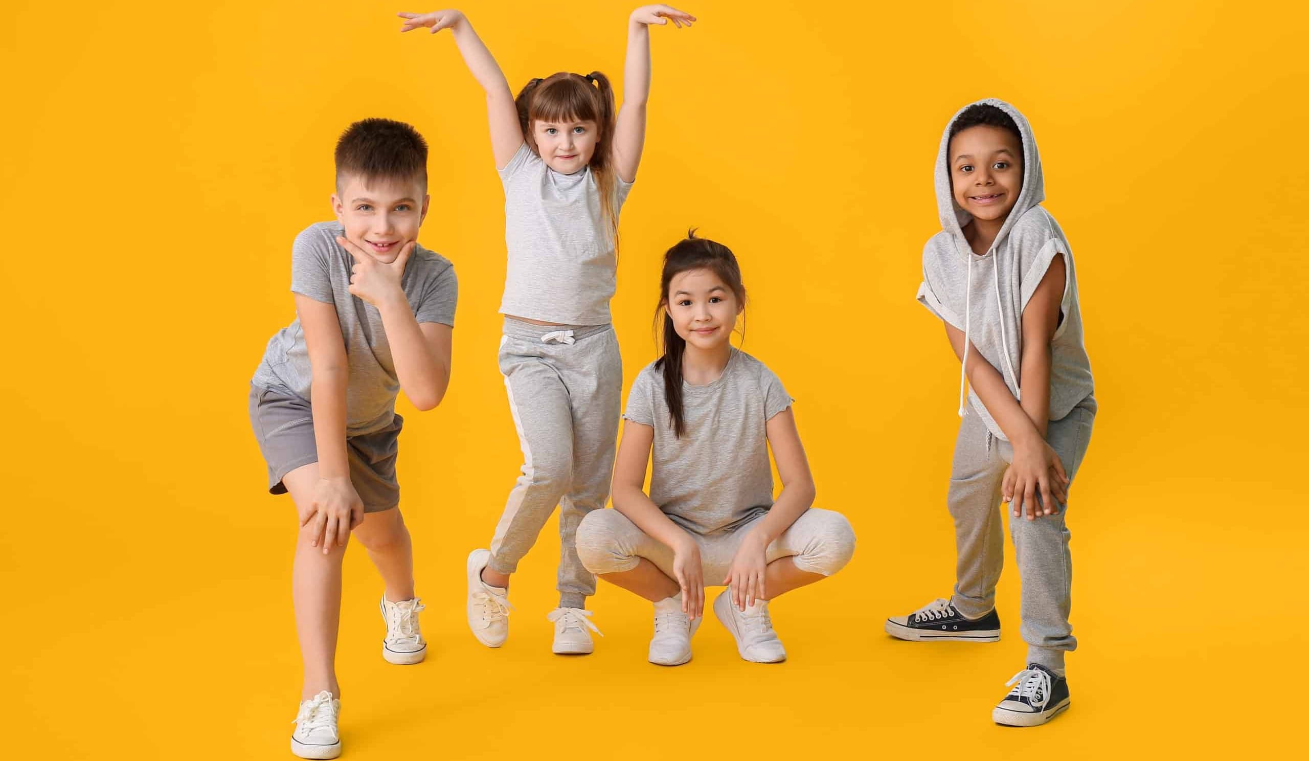 Four kids in grey dancewear striking hip hop and ballet poses against a yellow backdrop